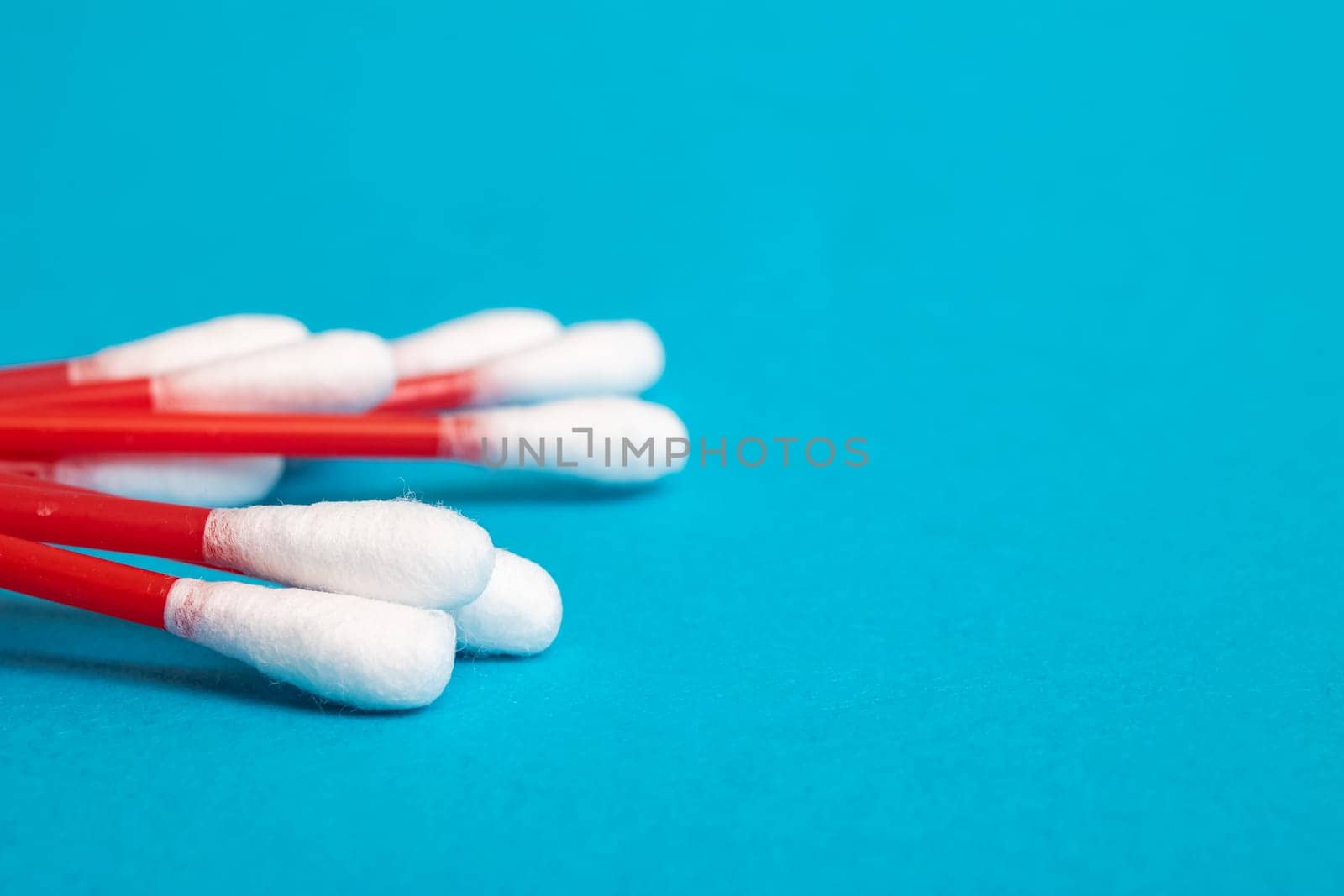 A pile of red cotton buds on a blue background close up, copy space
