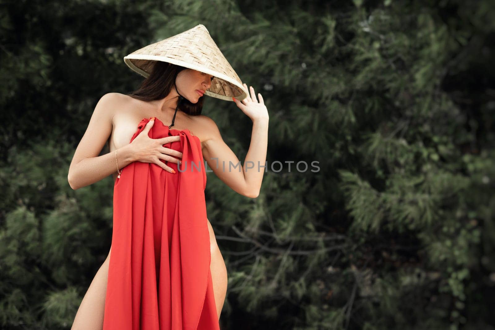 naked sexy woman in red fabric and Asian triangular hat on the background of nature by Rotozey