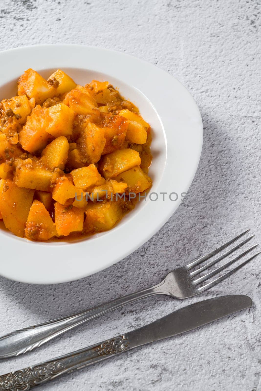 Minced meat and potato dish on white porcelain plate on stone table