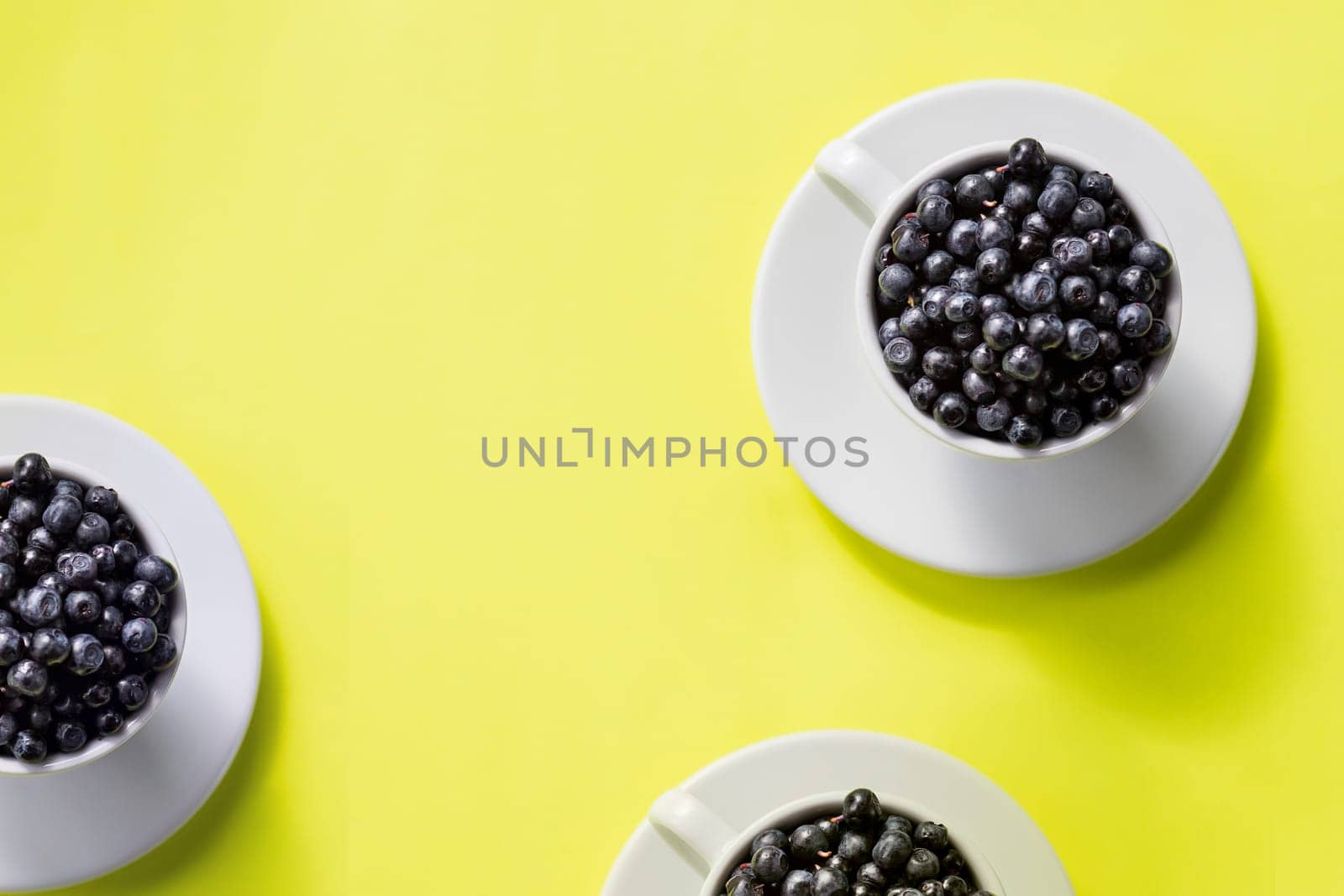Fresh raw organic farm blueberry in white cup on yellow kitchen background, copy space.Summer seasonal natural vitamines and antioxidants. Healthy diet and nutrition concept.flat lay by YuliaYaspe1979
