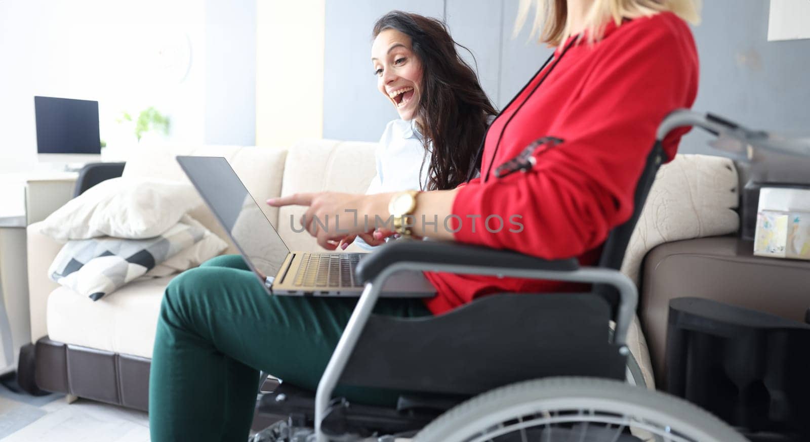 Friends spend time at home, watching movie and laughing, woman in wheelchair with laptop on lap by kuprevich