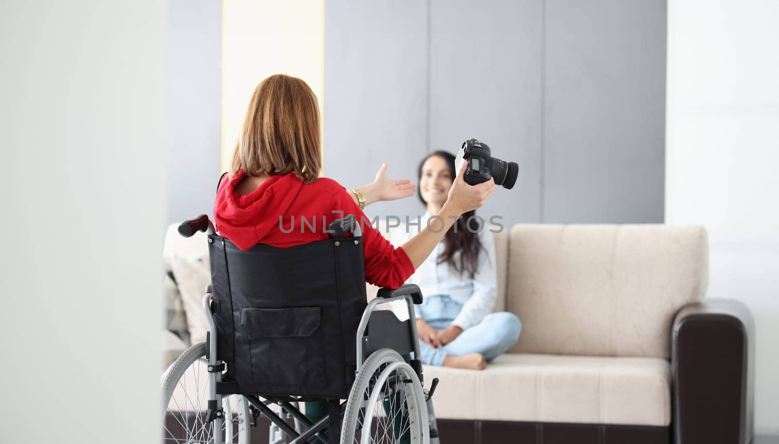 Portrait of professional photographer in wheelchair give advice on posing to model on sofa. Creative artist with photocamera. Disabled people, art concept