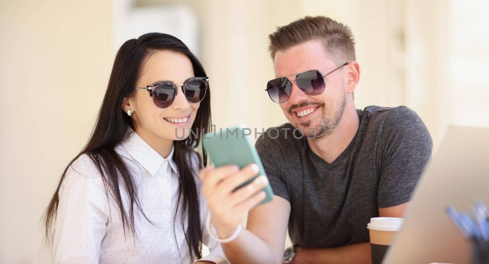 Portrait of couple watch memorable pictures on smartphone, go through pics from holiday. Man and woman smile, warm memories. Happiness, memory concept