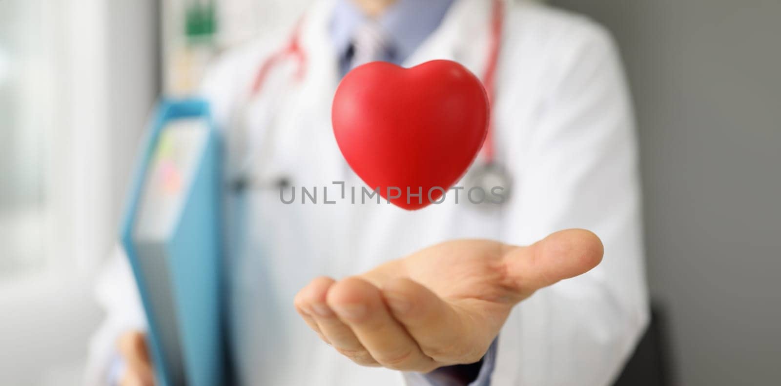 Close-up of cardiologist throw red plastic heart and catch it in palm, save life through donation or charity activity. Medicine, cardiology, health concept