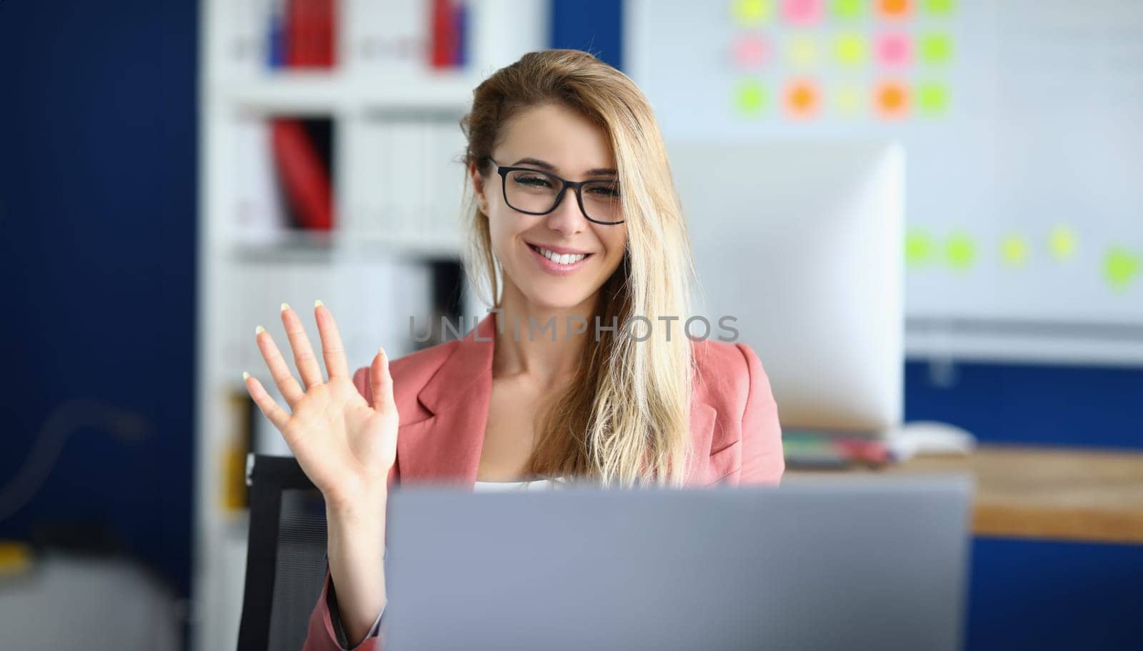 Portrait of pretty businesswoman greeting coworkers on video call in cabinet. Employee in suit, online meeting with colleagues. Corporate, business concept