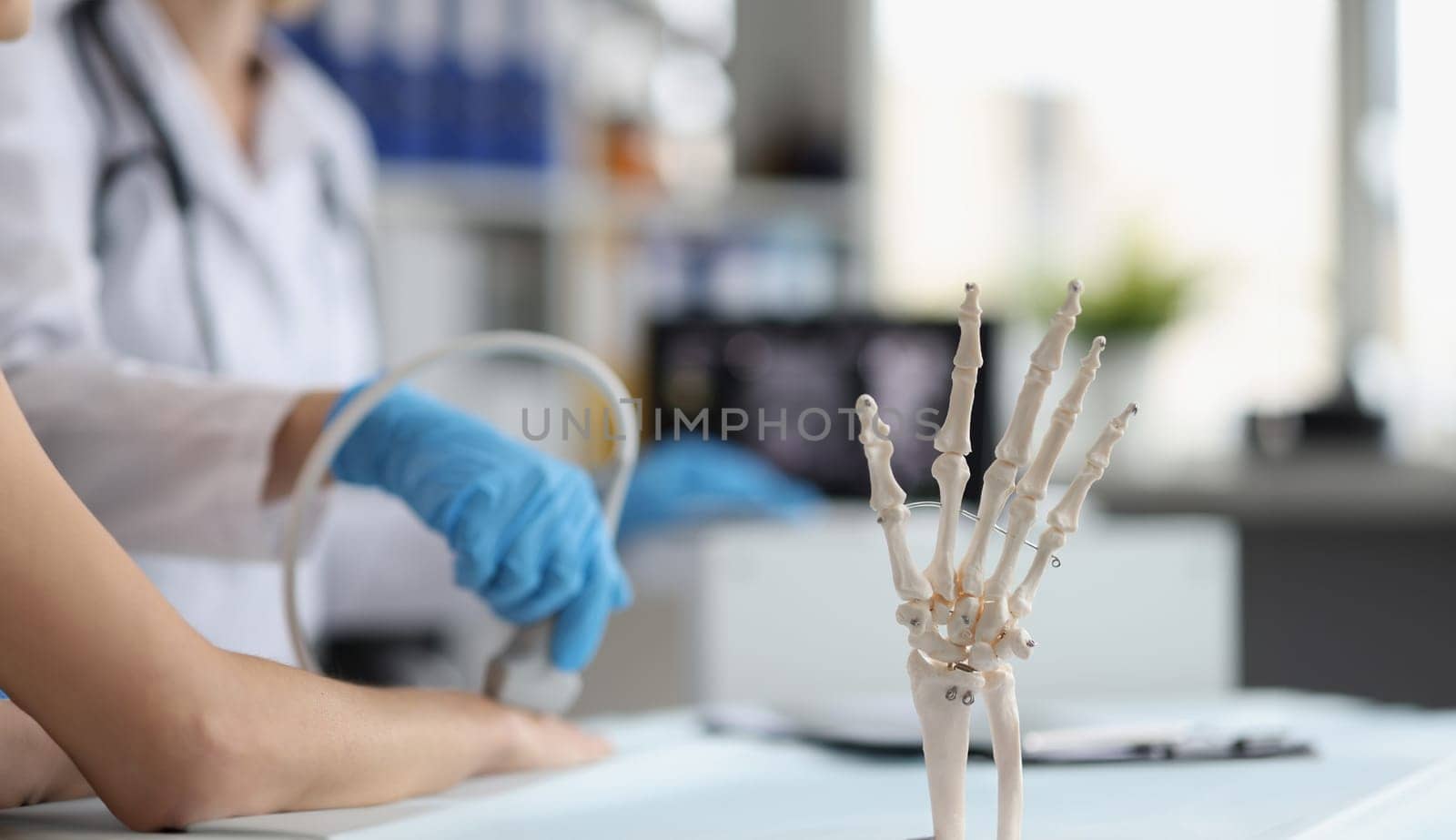 Close-up of doctor do ultrasound of hand, skeleton hand model on desk, medical anatomy science. Medicine, biology, lab, healthcare, injury, clinic concept