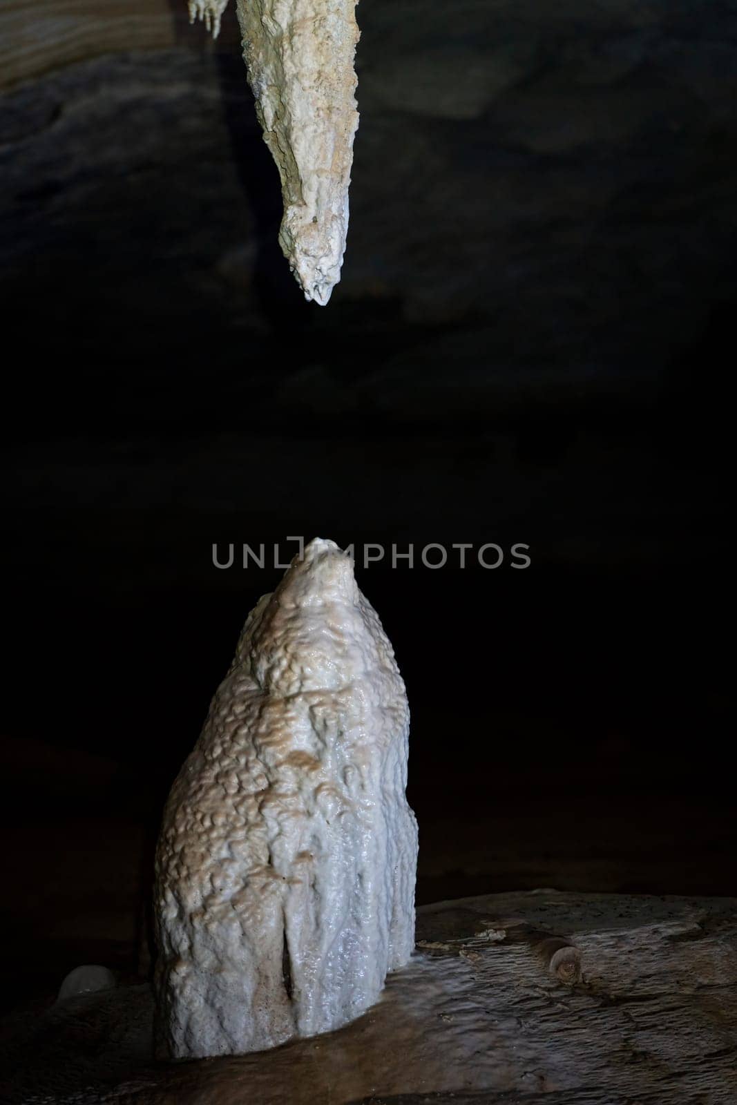 A photo shows a stalactite and stalagmite nearing union in the quiet of a cave.