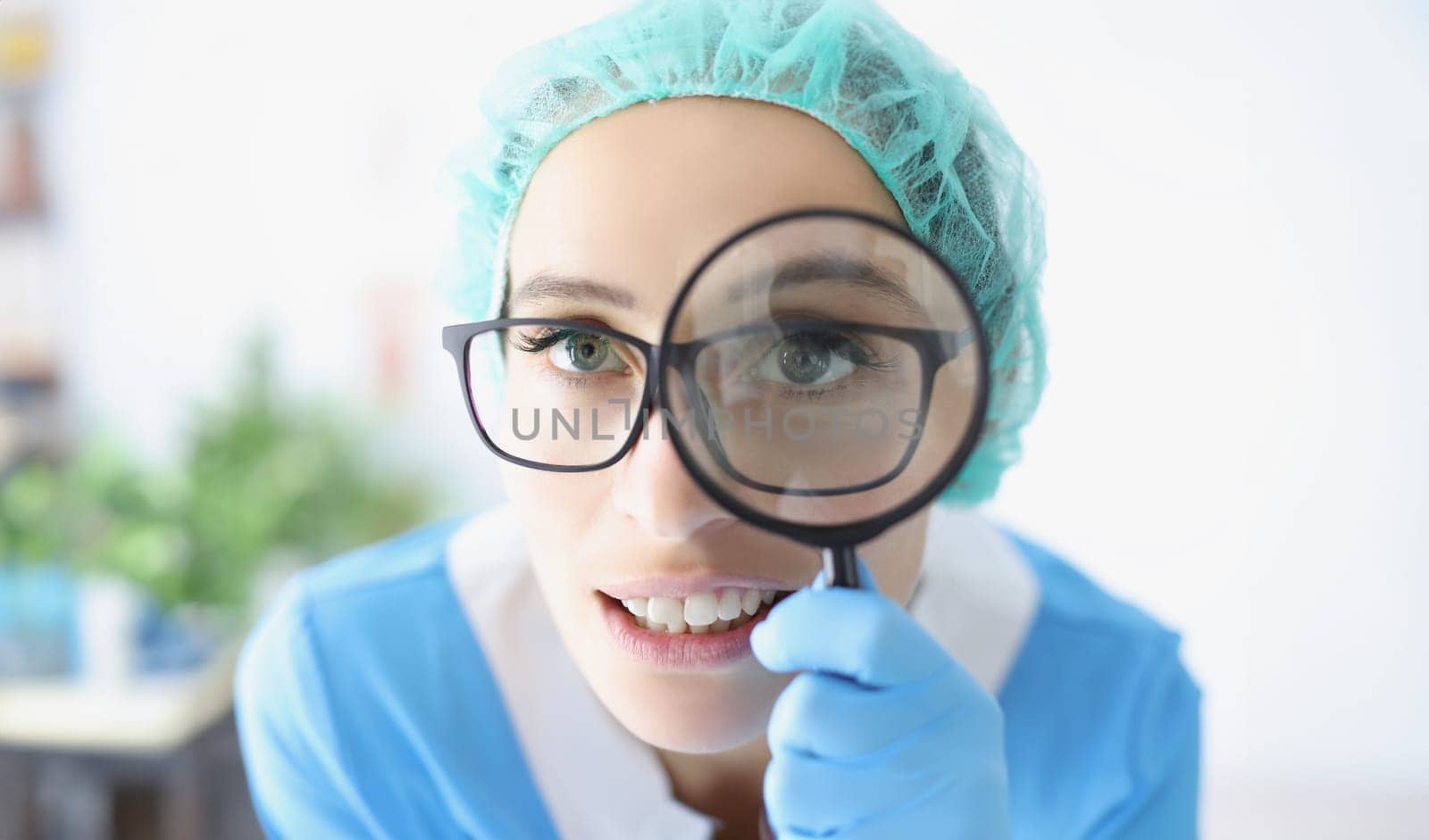 Portrait of doctor in glasses looks through magnifying loupe, intern provide investigation in clinic. Medical worker use magnifying glass. Medicine concept