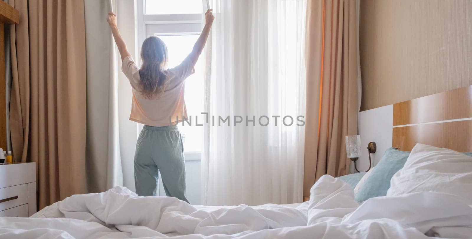 Woman stretching standing by window after wake up, back view by Desperada