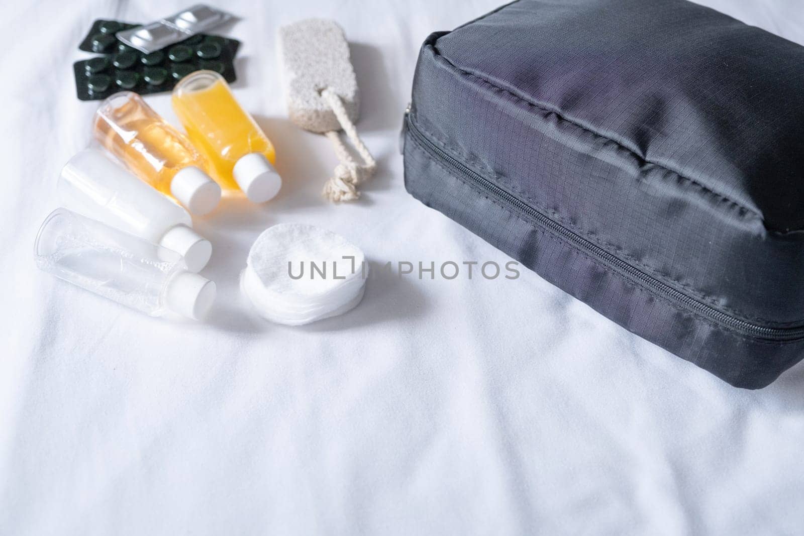 Travel cosmetics kit with bottles, pills and cosmetics on bed , top view