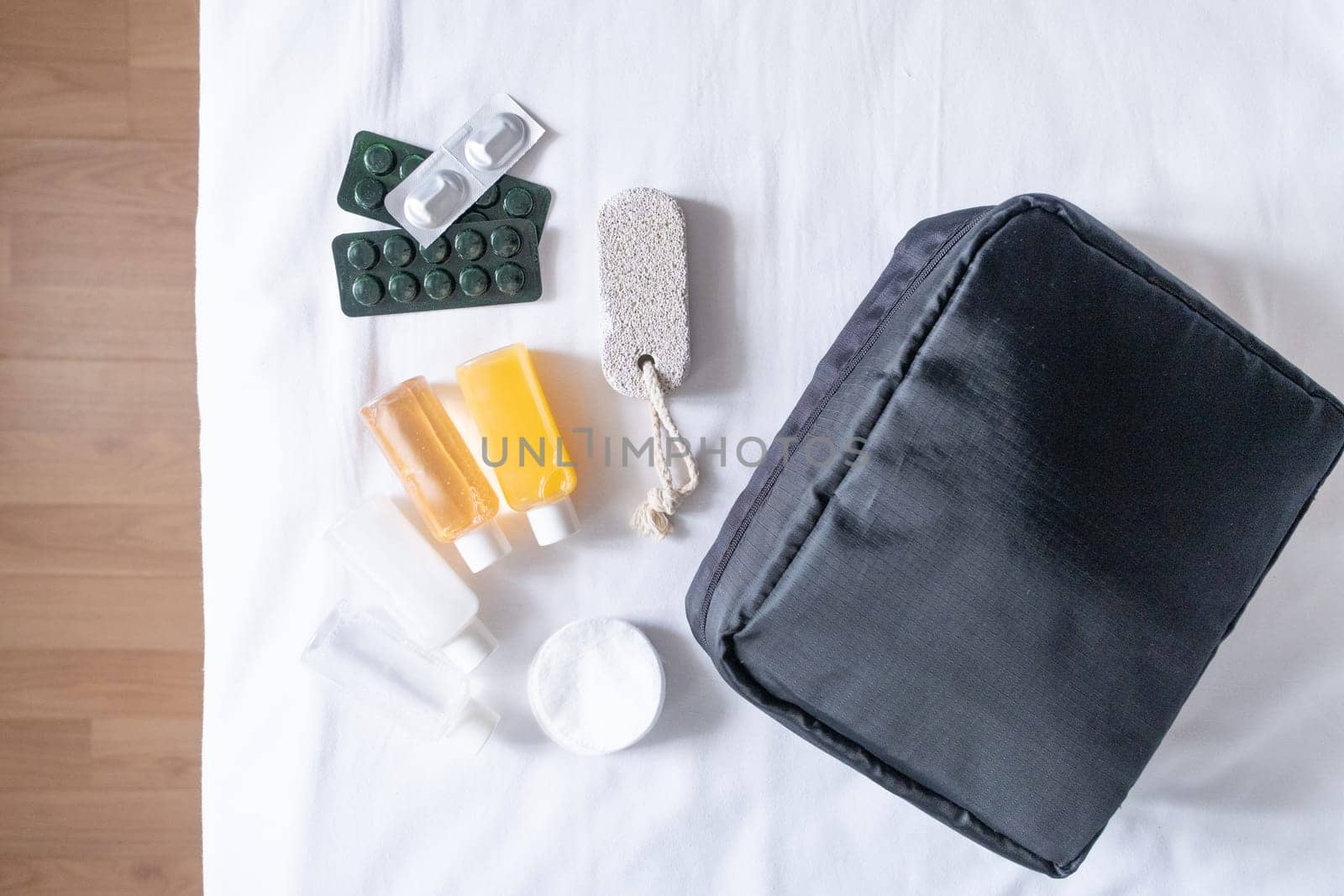 Travel cosmetics kit with bottles, pills and cosmetics on bed , top view