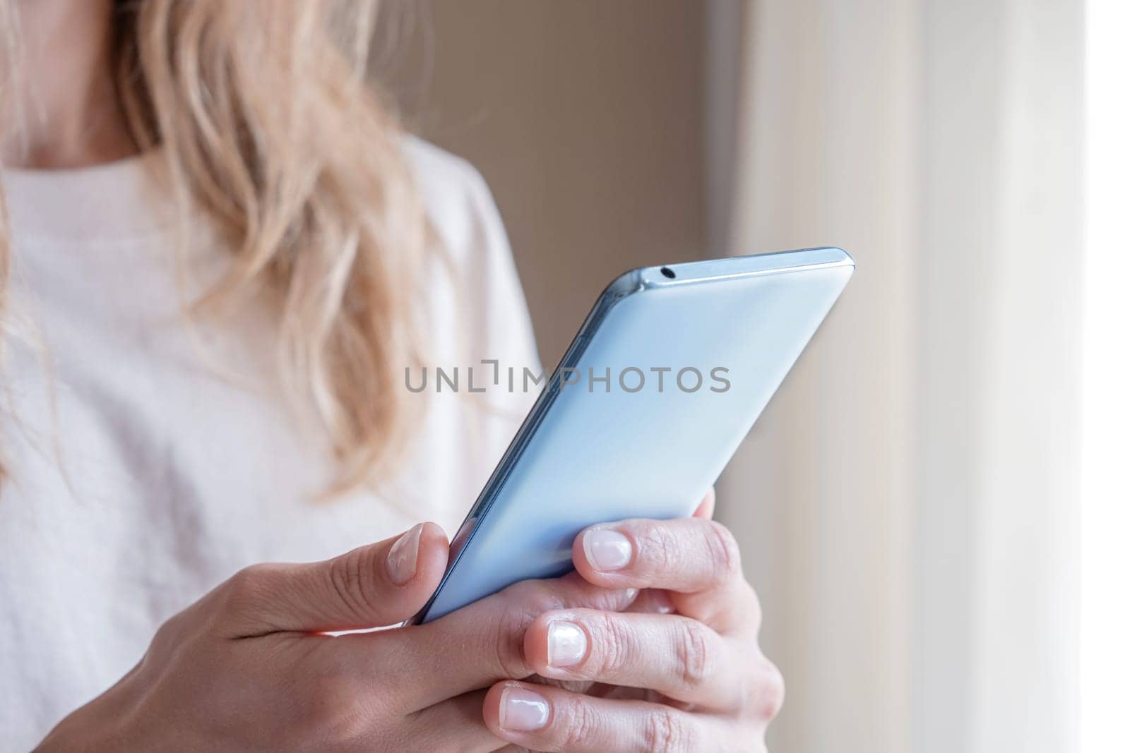 closeup of unrecognizable person in home clothes using phone standing by the window in hotel room