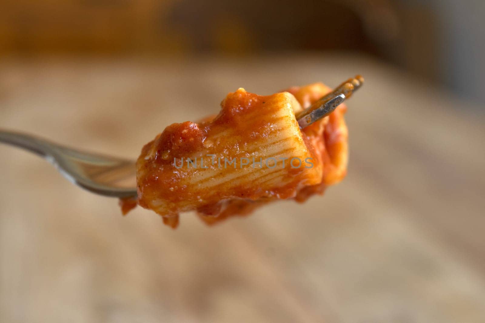 fork with rigatoni with tomato sauce and in the background a plate of pasta with sauce