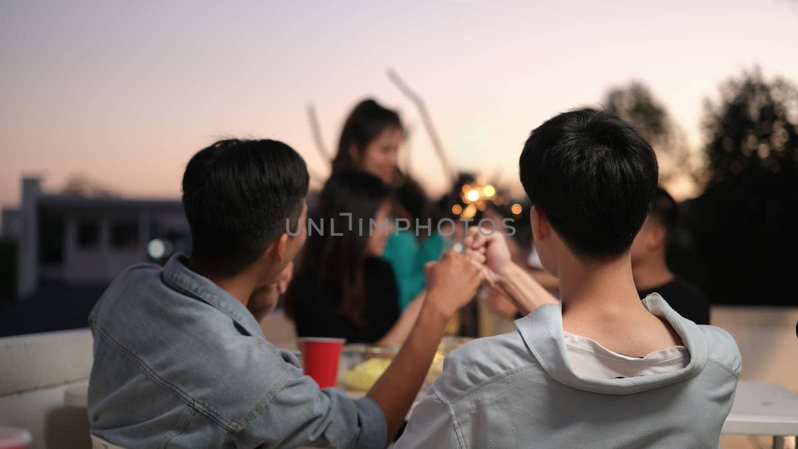 Group of friends taking and enjoying drinks during rooftop party at sunset. by prathanchorruangsak