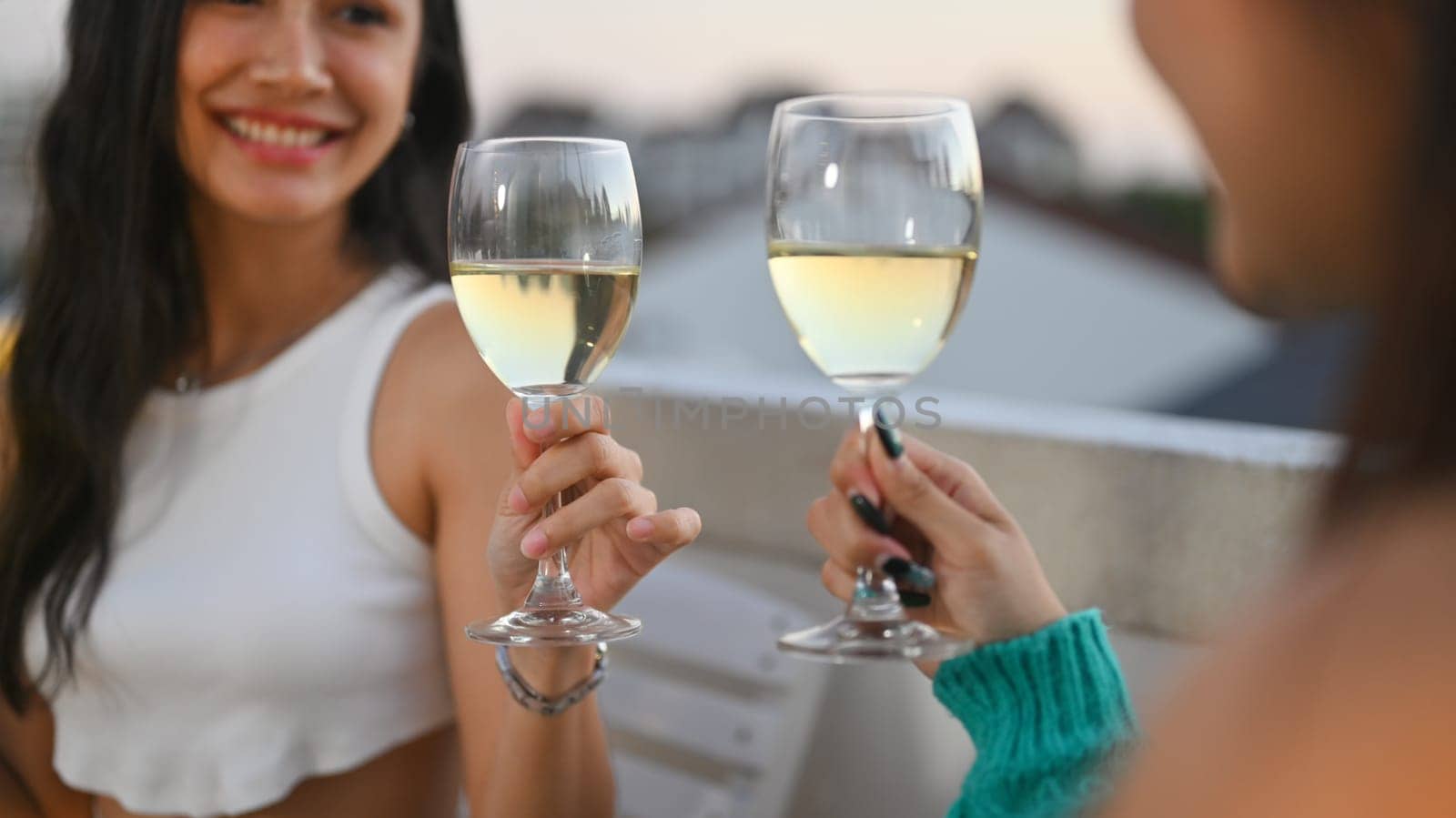 Cheerful Asian female friends toasting white wine celebrating together at rooftop dinner party by prathanchorruangsak