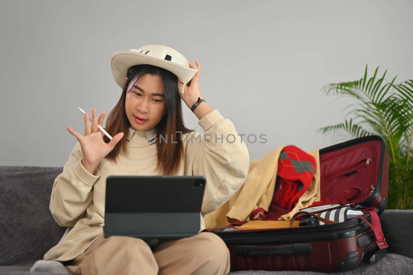 Young woman having video call on digital tablet while preparation for a vacation trip at home.