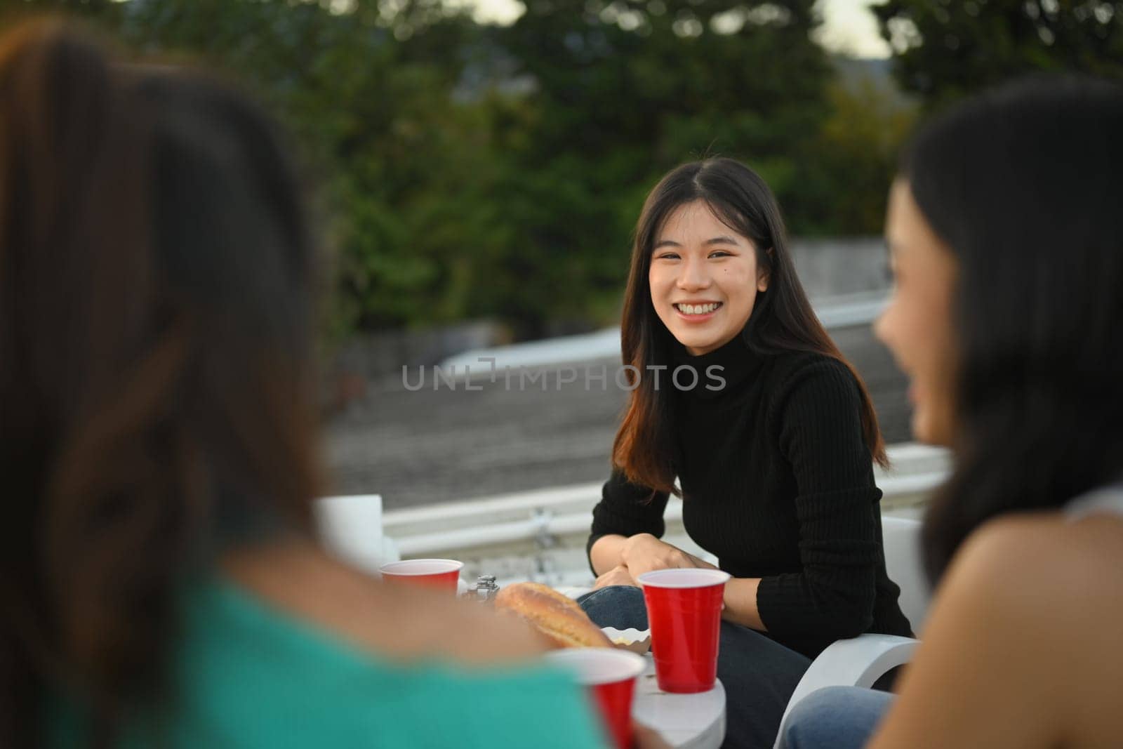 Attractive young woman talking with friends during rooftop party. by prathanchorruangsak