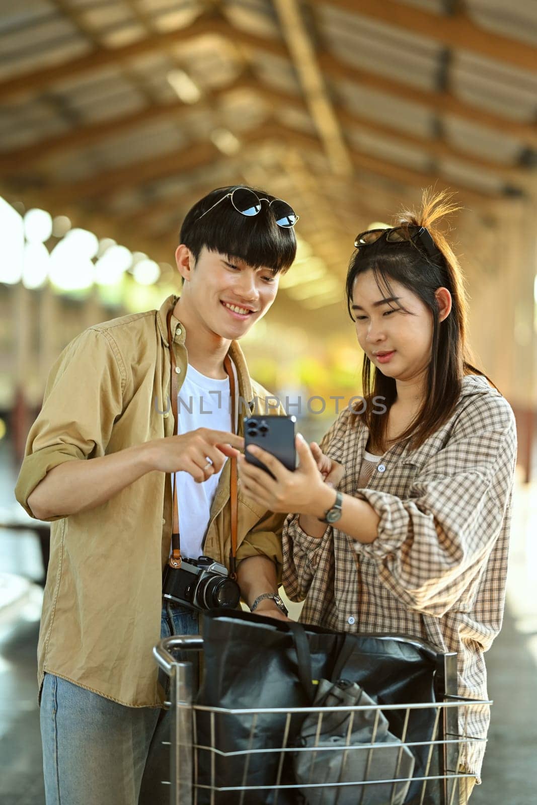 Happy young couple using mobile phone during waiting for the train at station.