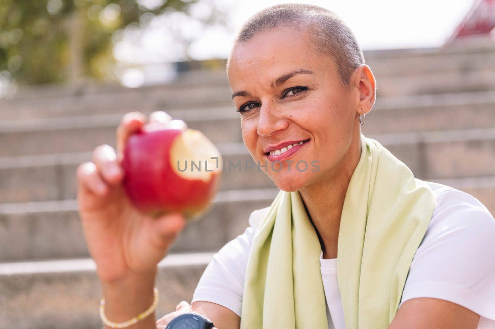 happy sports woman showing a bitten apple after workout, concept of healthy and active lifestyle, focus on the smiling face