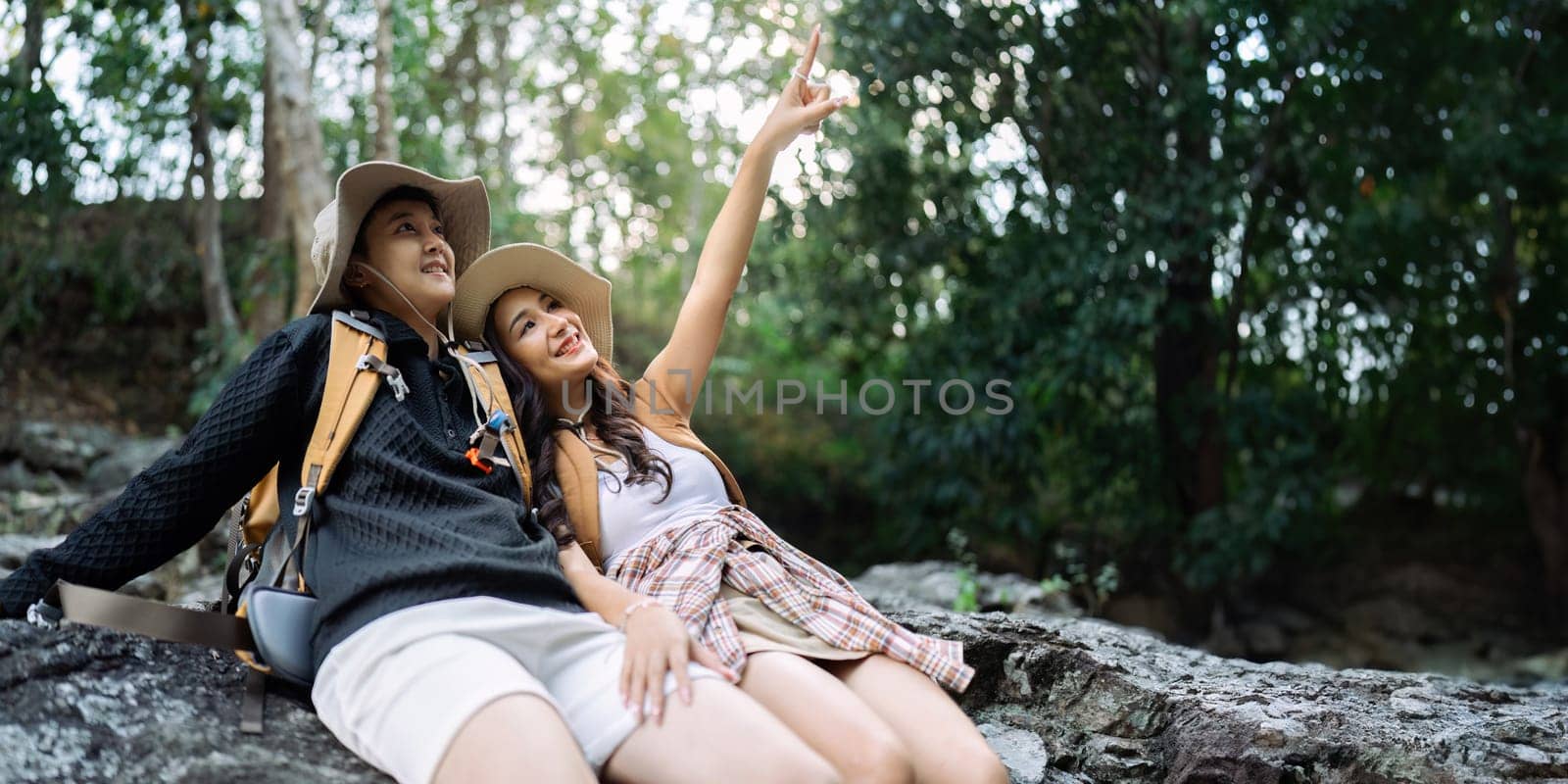 Lesbian couple relaxing together on rock at a hiking trail While traveling together on a hiking trail.