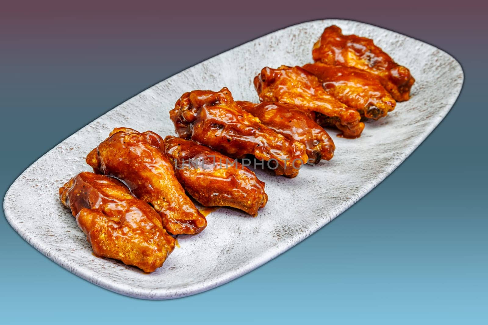 Composition of a plate of chicken wings with barbecue sauce on a magenta and light blue gradient background