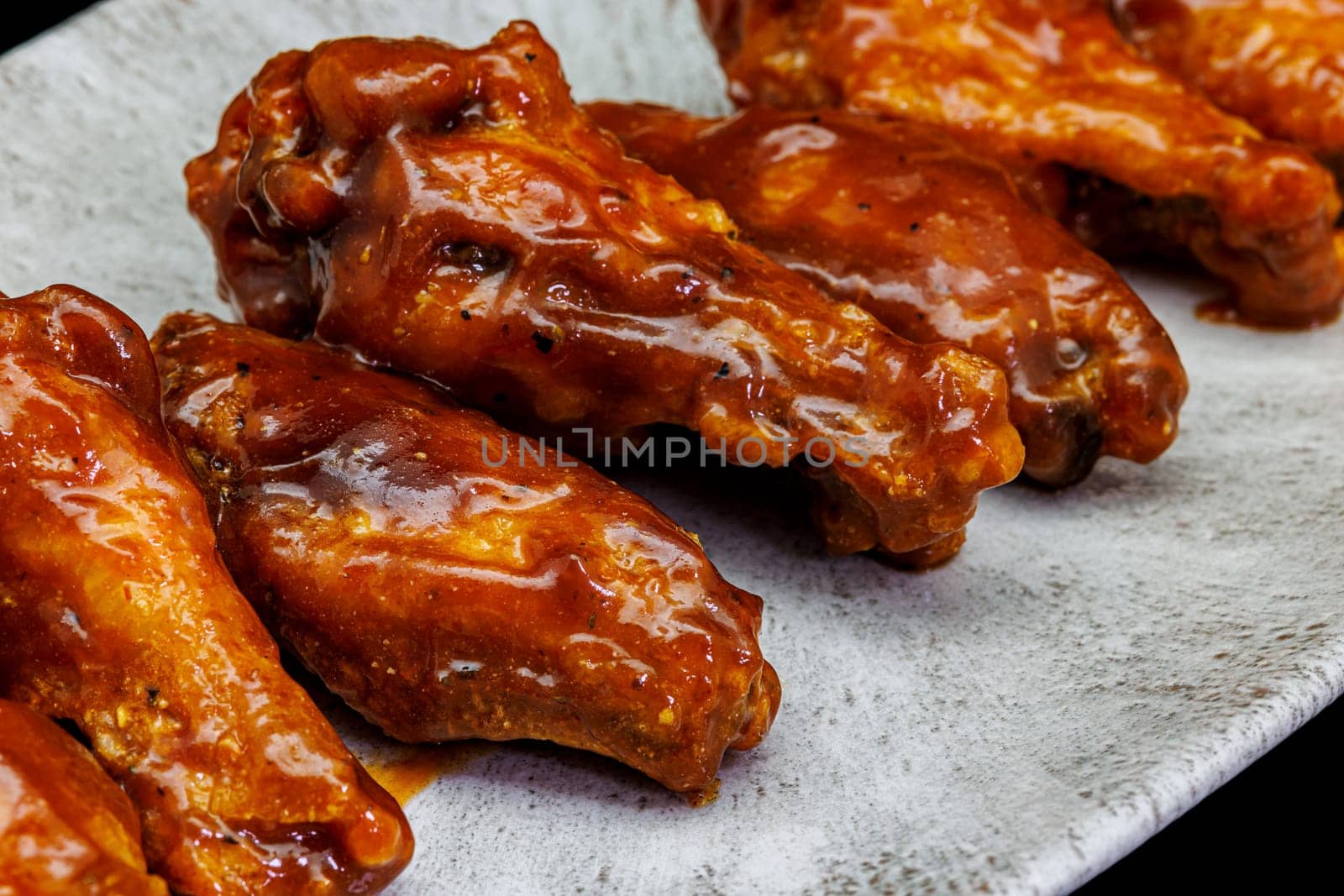 Composition of a plate of chicken wings with barbecue sauce on black background