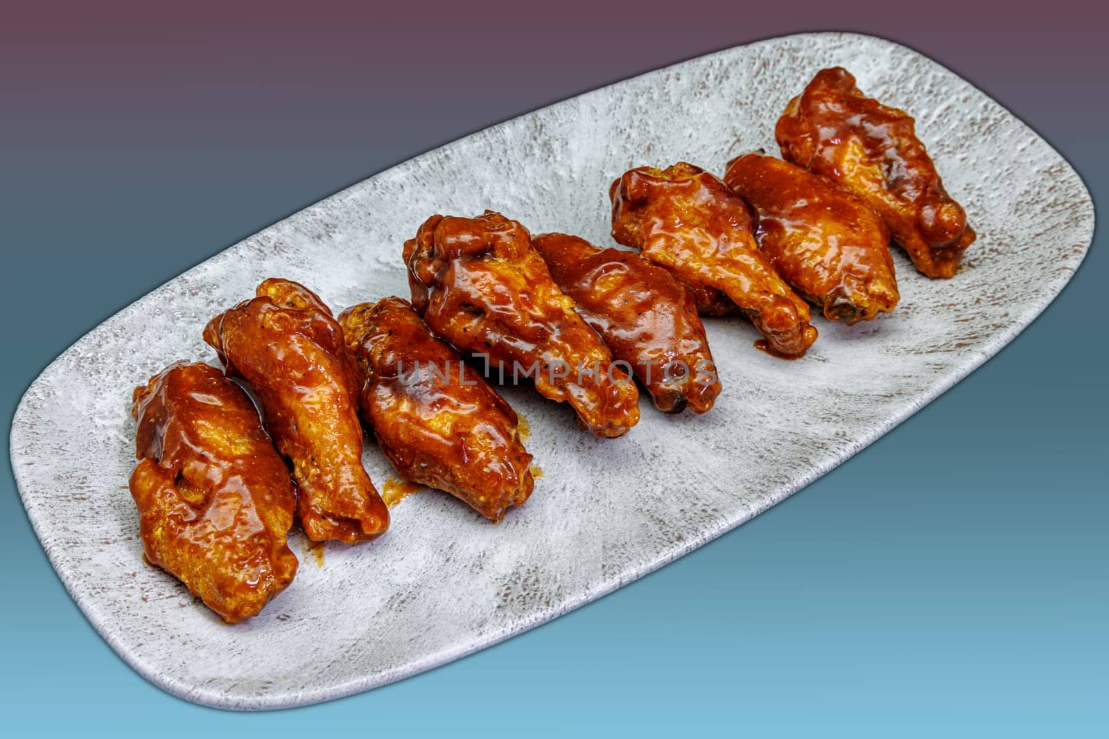 Composition of a plate of chicken wings with barbecue sauce on a magenta and light blue gradient background