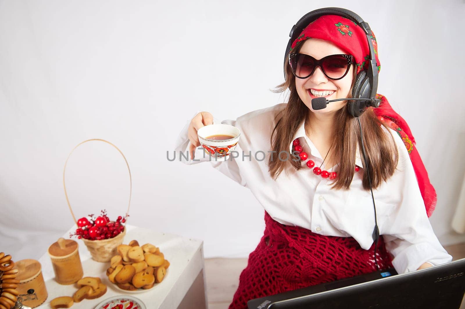 Portrait of young girl in a bright red scarf and large headphones with a microphone. A woman who is radio or television presenter with cap of tee. Funny female telecom operator. Freelancer at work