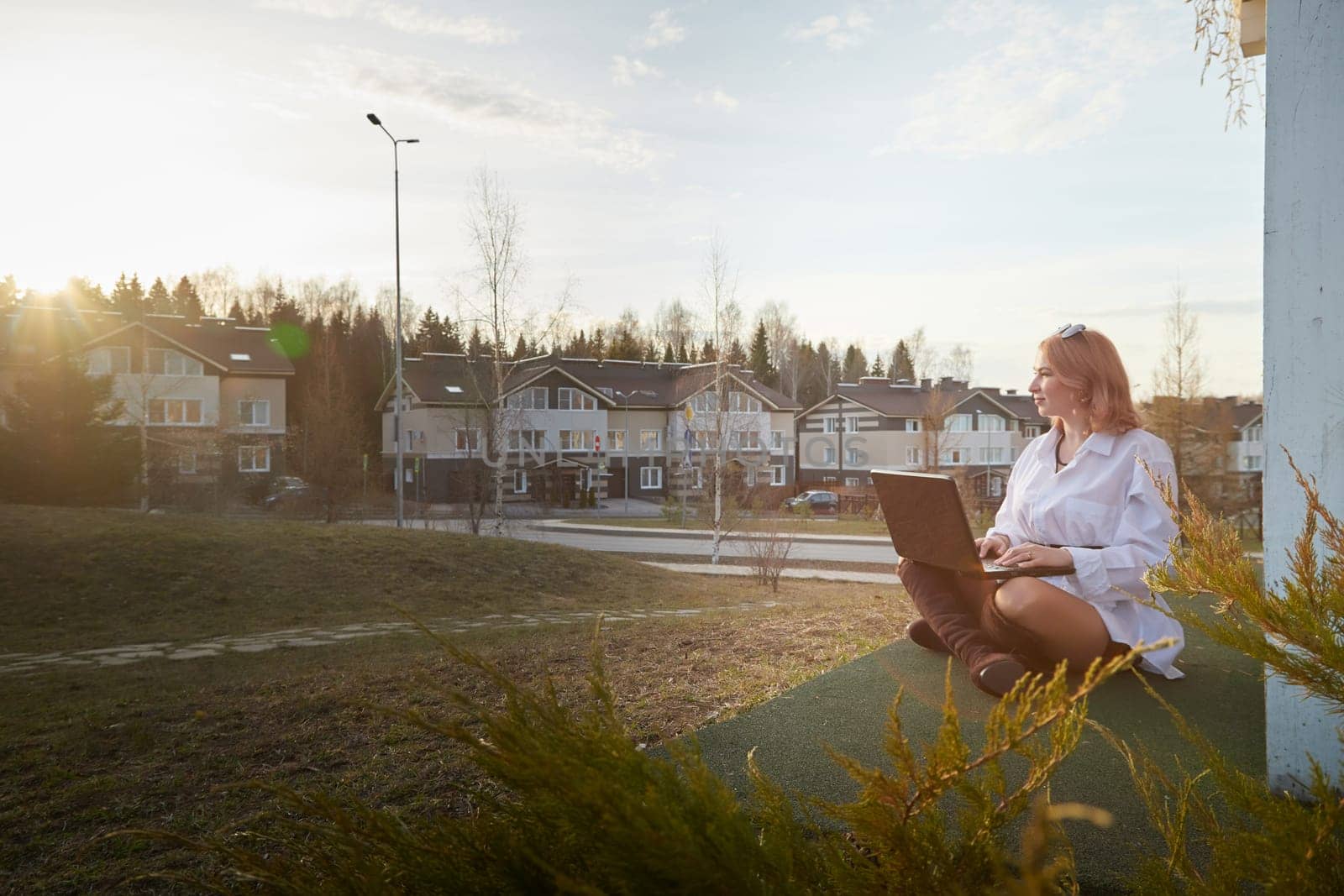 Beautiful redhead moden girl working by laptop in gazebo on autumn, summer or spring day. Businesswoman, student, freelancer or manager works outdoors in natural landscape in a village, city or town