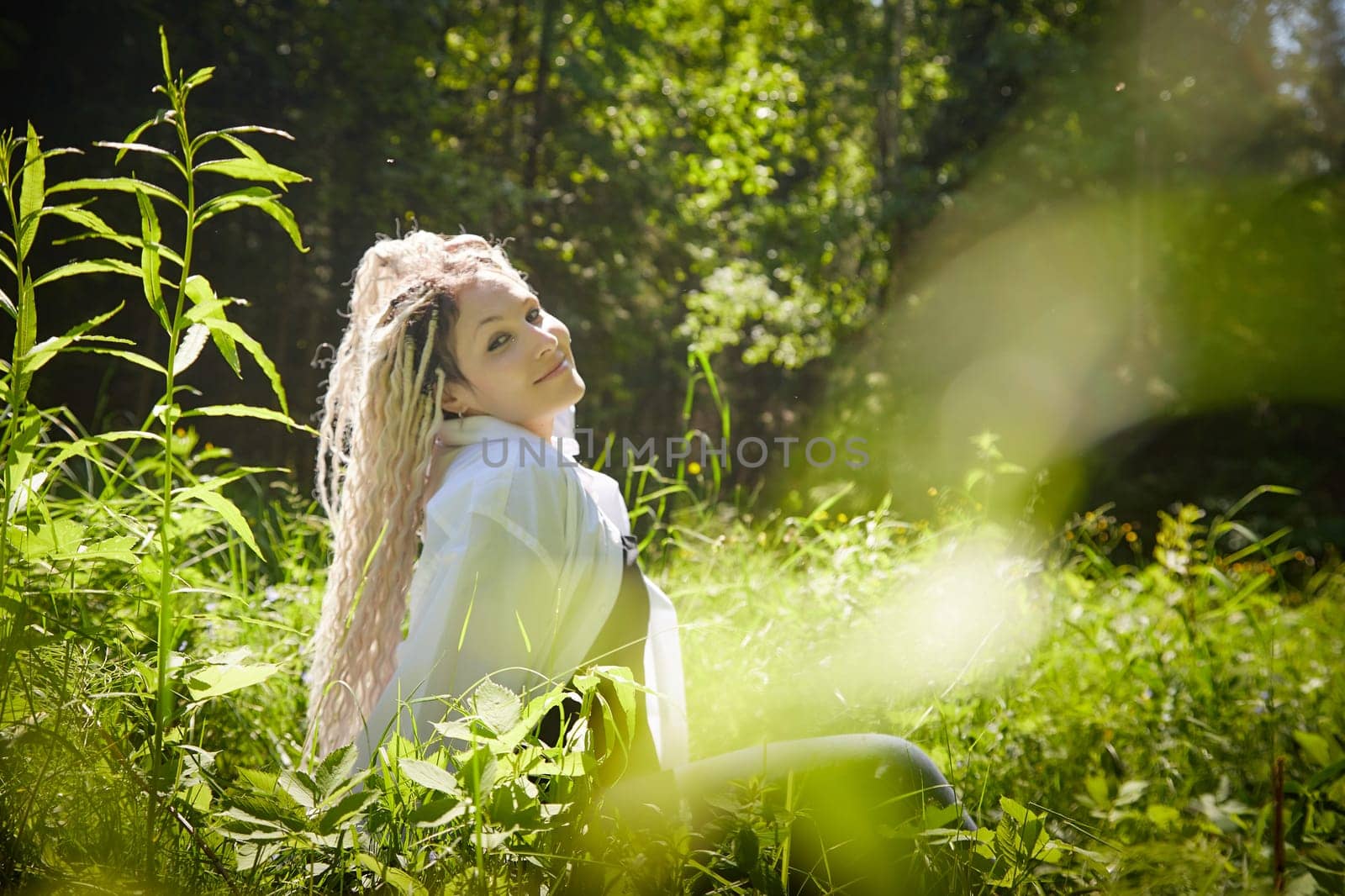 Hippy girl enjoys life in forest on a sunny spring or summer day. Woman in green nature landscape