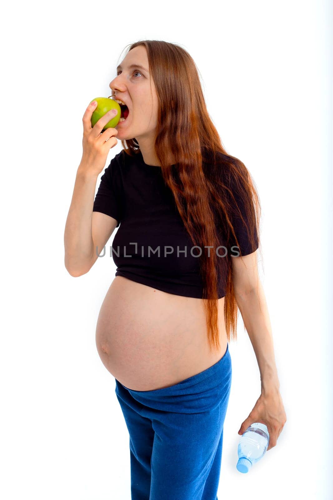 Pregnant woman propose apple for her belly copy space. Beautiful expectant lady having fresh snack, gray studio background. Healthy nutrition and pregnancy concept