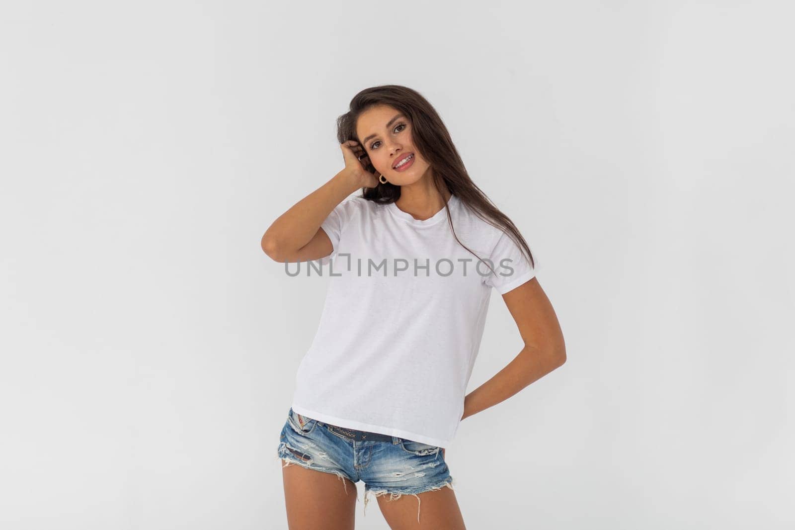 Beautiful brunette girl in a white T-shirt and denim shorts posing on a white background. High quality photo