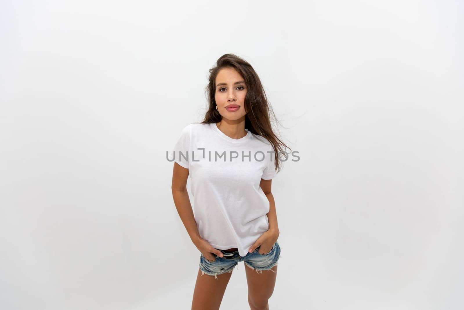 Beautiful brunette girl in a white T-shirt and denim shorts posing on a white background. High quality photo