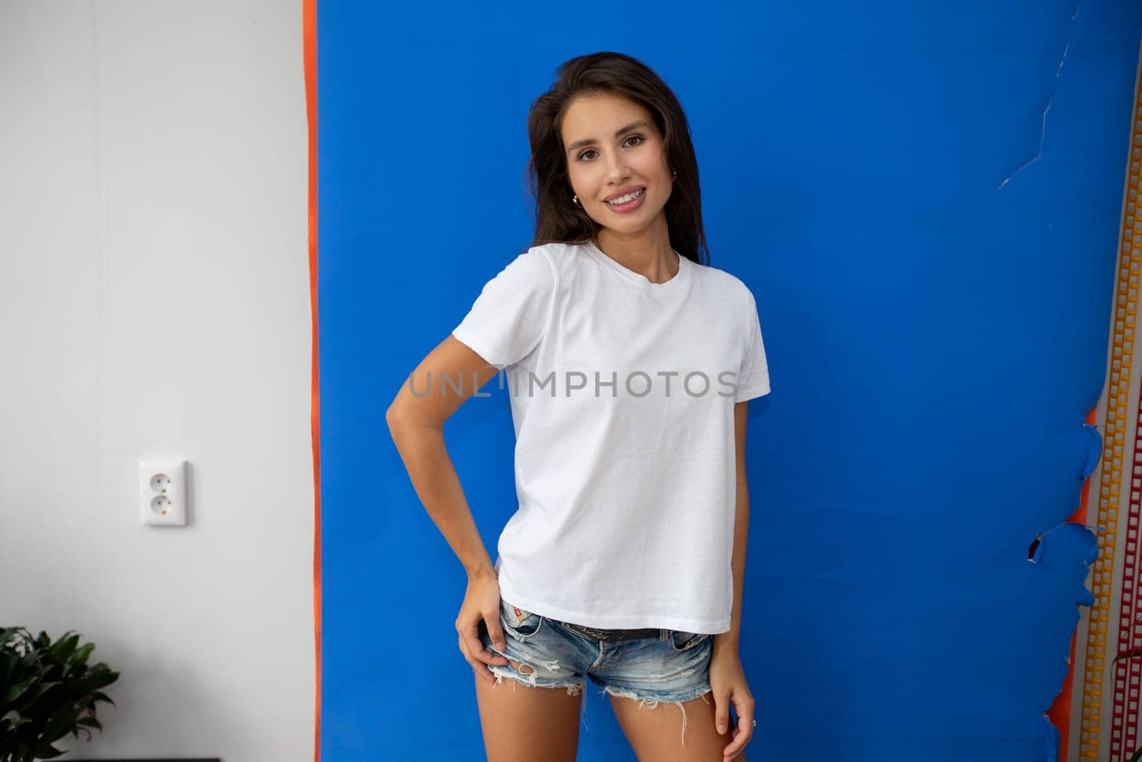 Beautiful brunette in a white T-shirt and shorts posing on a blue background. High quality photo