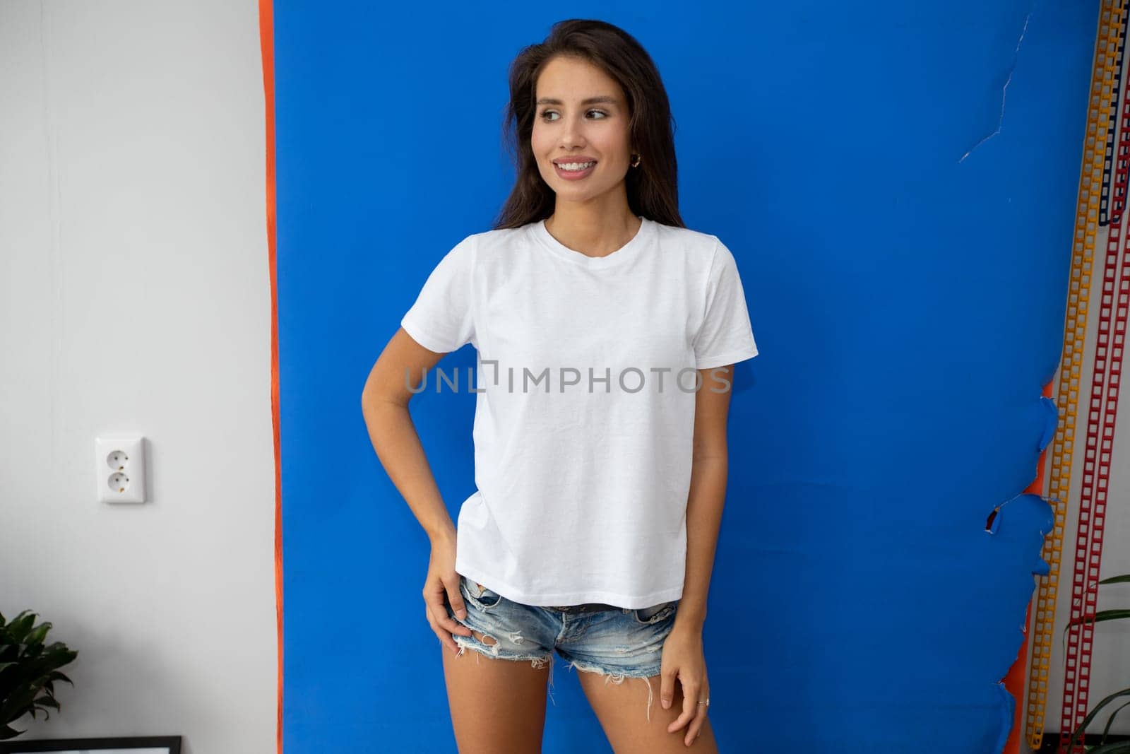 Beautiful brunette in a white T-shirt and shorts posing on a blue background by Freeman_Studio