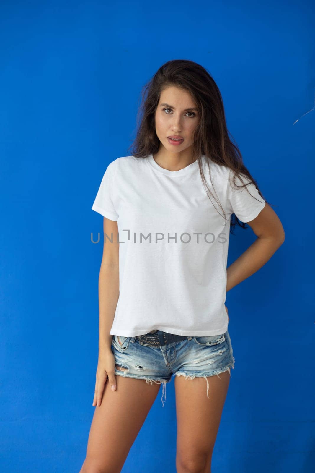 Beautiful brunette in a white T-shirt and shorts posing on a blue background. High quality photo