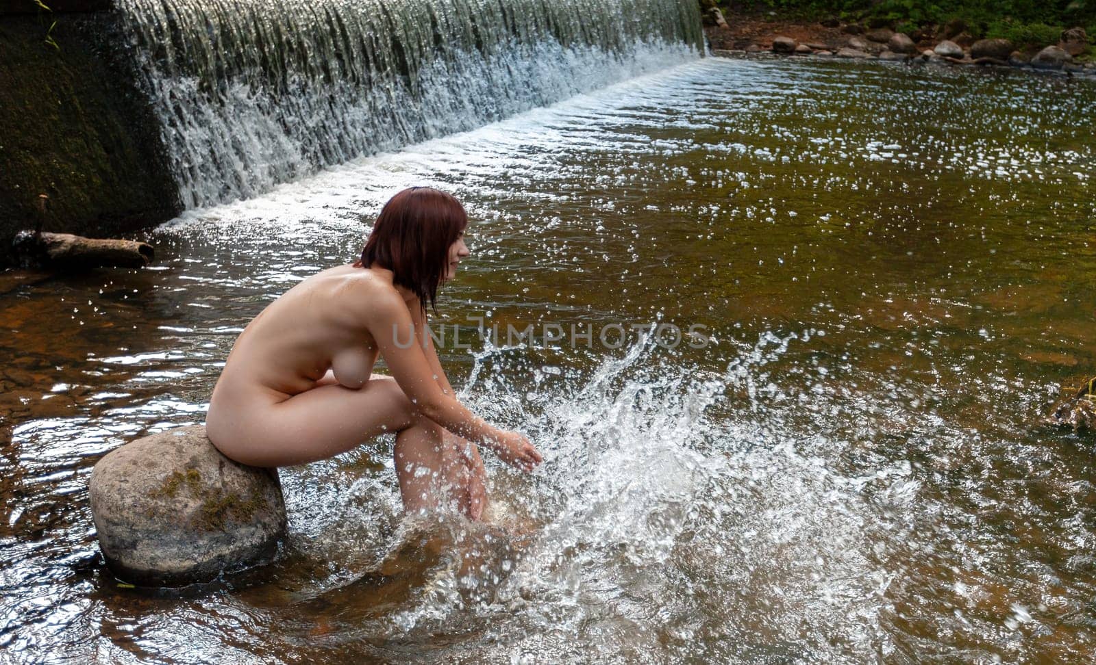 Young nude woman enjoying the fresh coolness near a forest stream with a waterfall