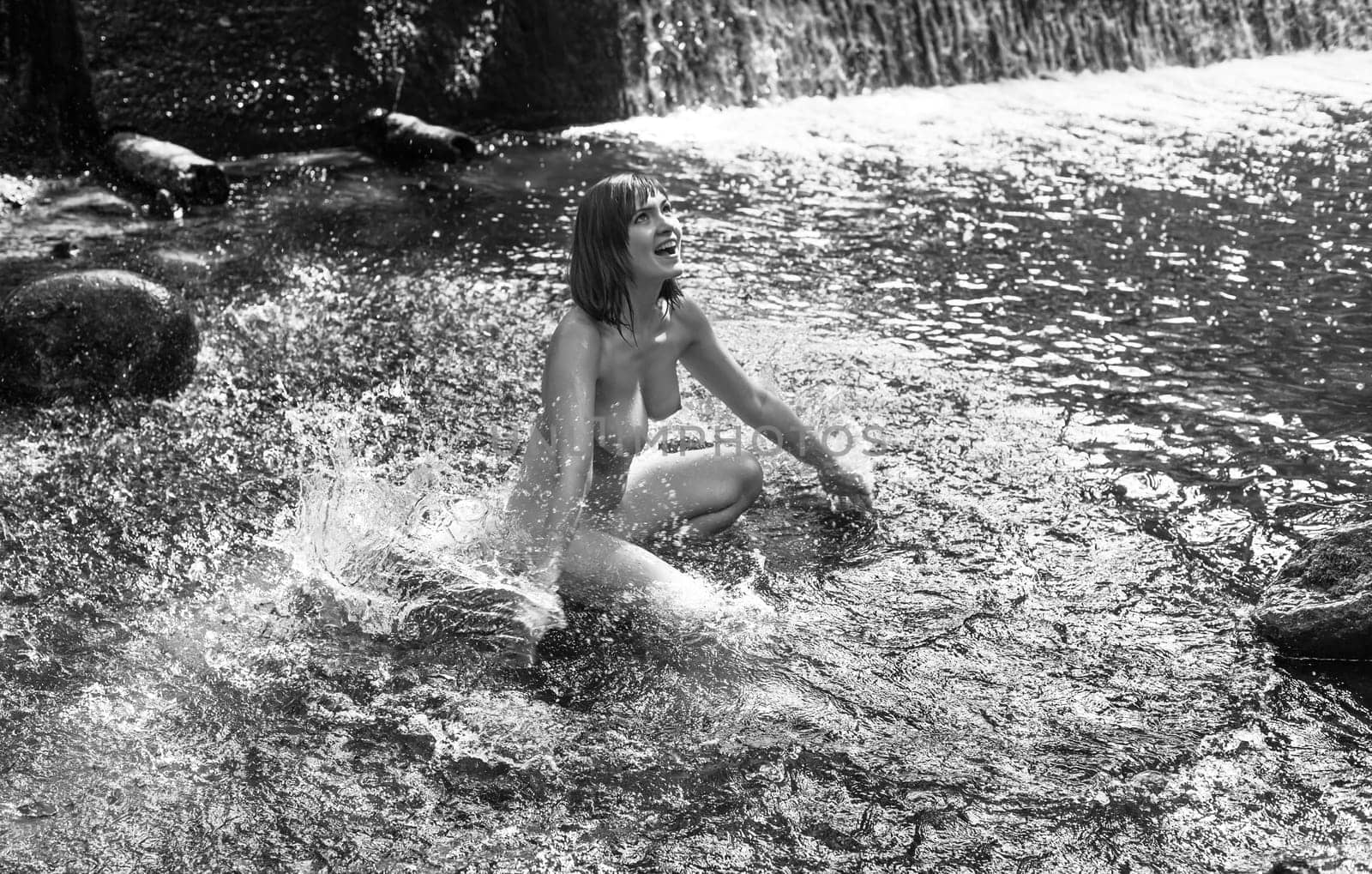 Young nude woman enjoying the fresh coolness near a forest stream with a waterfall