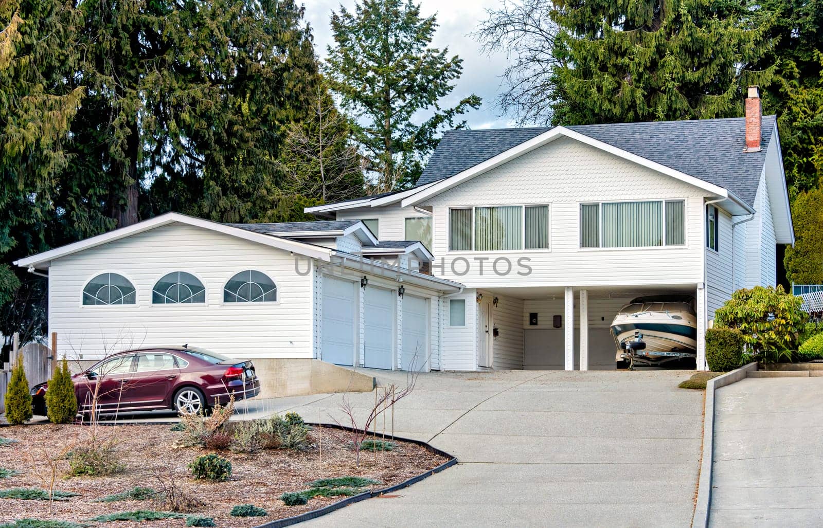 Suburban family house with small boat on trailer parked under carport. Big residential house with car parked on concrete driveway.