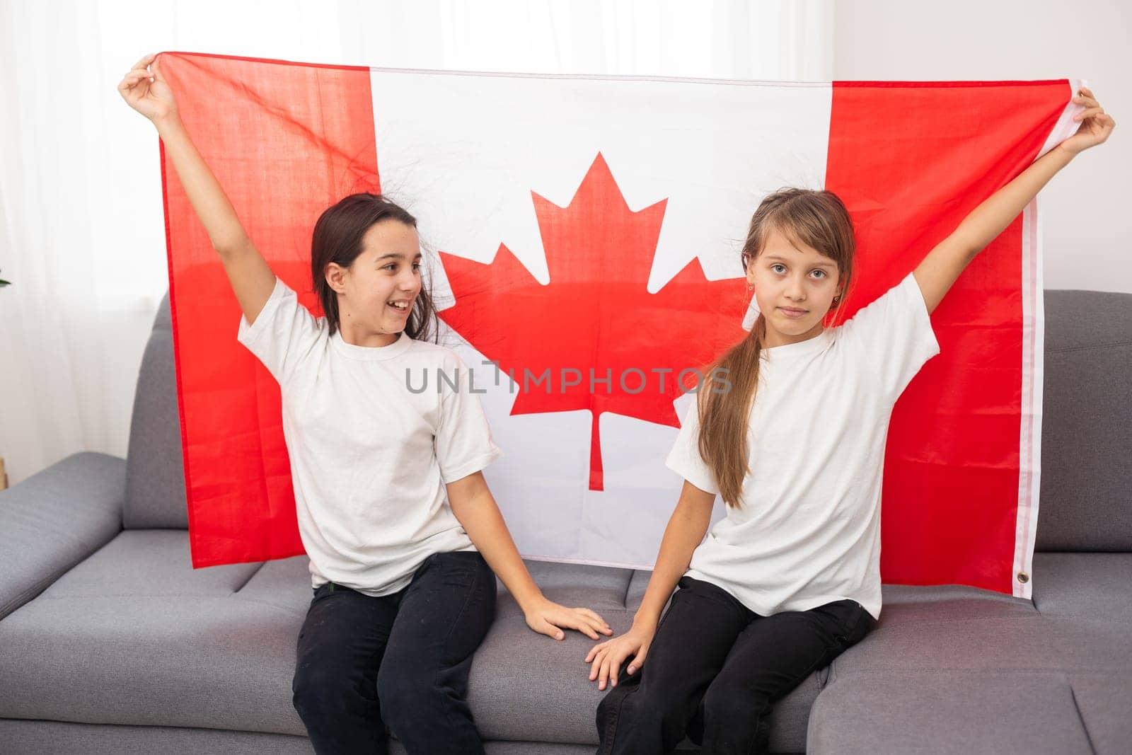 Happy Canada Day Celebration. Two girls with braided hair are at nature background with big Canada flag in their hands. Young Canadian caucasian kids 1st of July. High quality photo