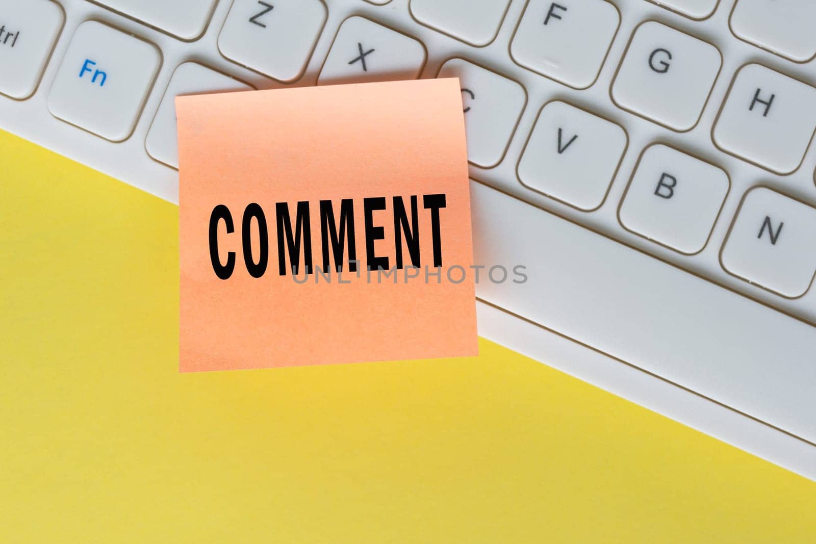 Comment text on orange sticky note on top of white keyboard. Social media marketing concept background.