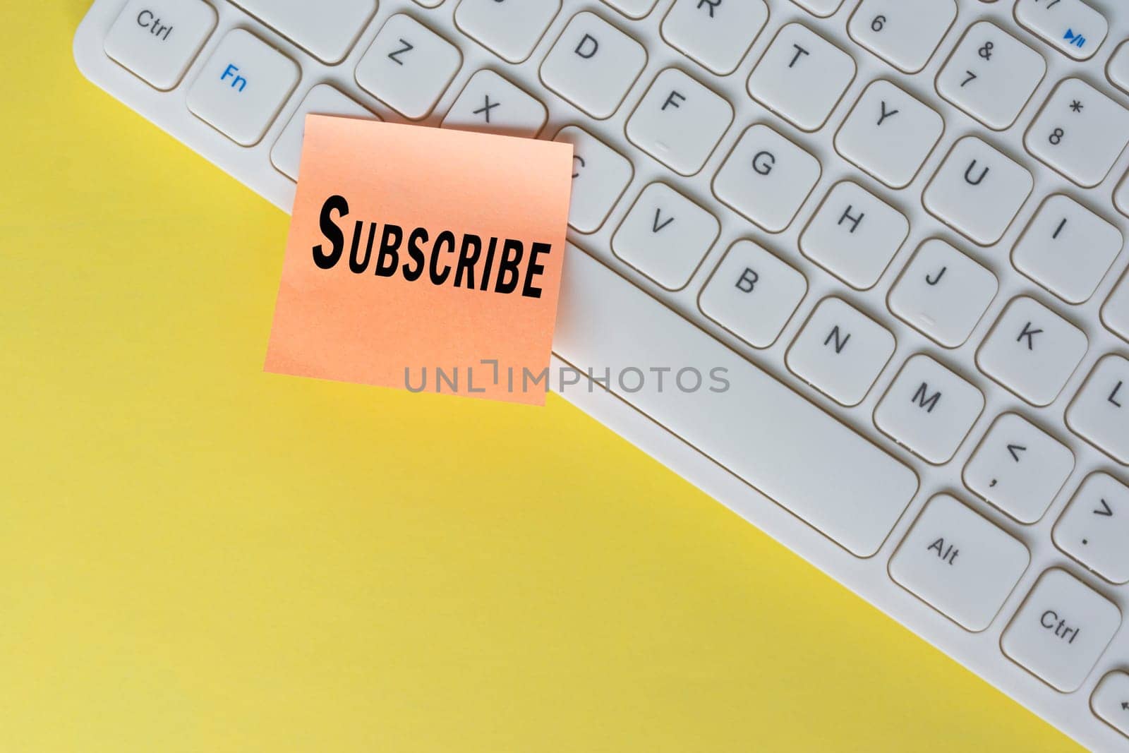 Subscribe text on orange sticky note on top of white keyboard. Social media marketing concept background.