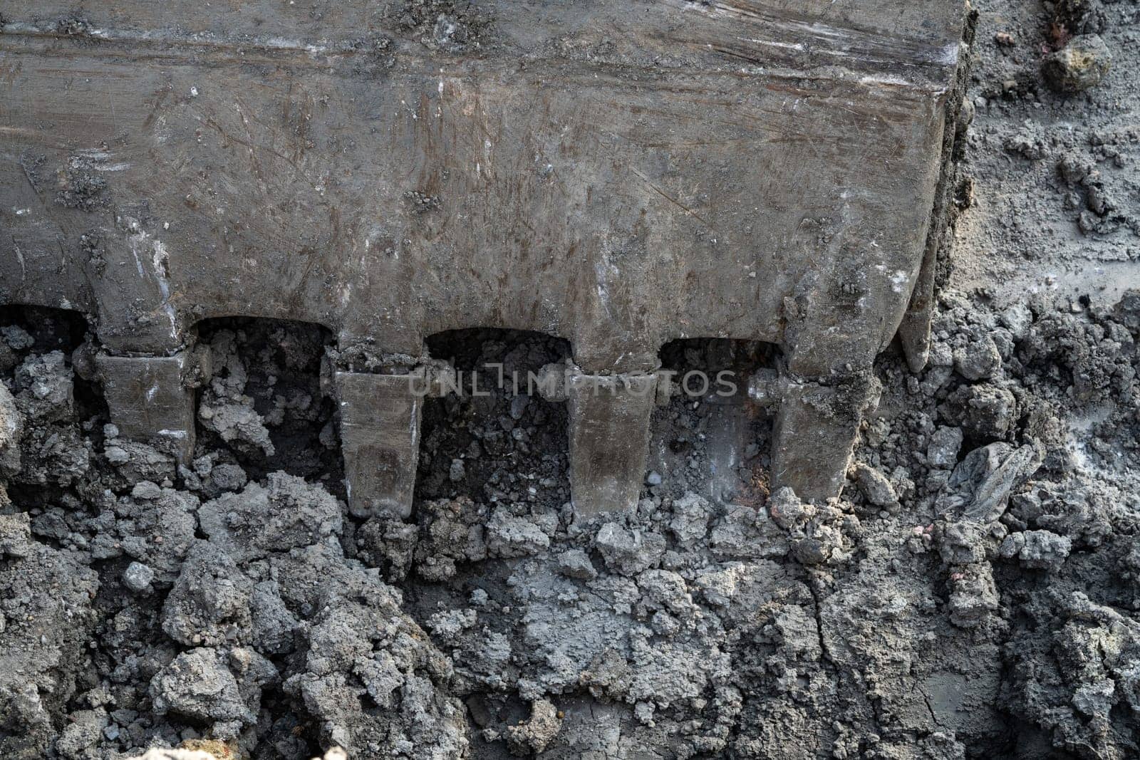 Closeup dirty bucket of backhoe working at construction site. Bucket teeth of backhoe digging soil. Crawler excavator digging on soil. Excavating machine. Earthmoving machine. Excavation vehicle. by Fahroni