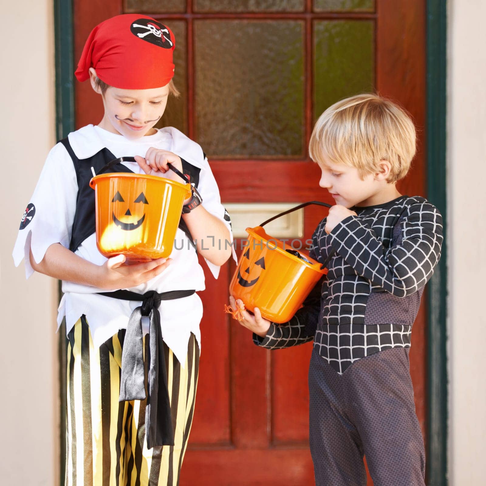 Halloween, candy and door with children in costume on porch for trick or treat celebration together. Friends, food and sweets with young boy kids in fancy dress for spooky holiday or vacation by YuriArcurs