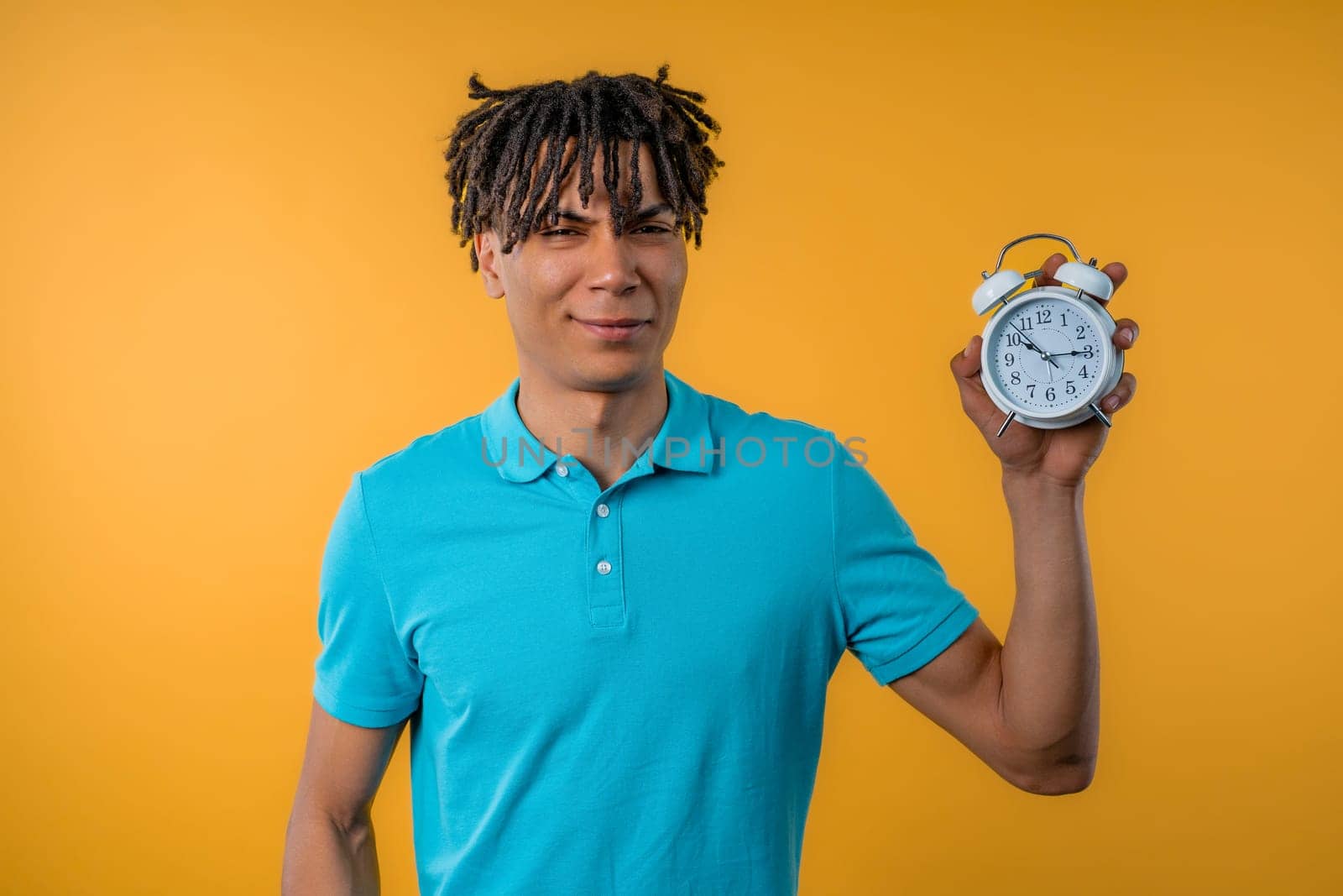 Woken up by alarm clock sleepy african man holding it in hand. Yellow background by kristina_kokhanova