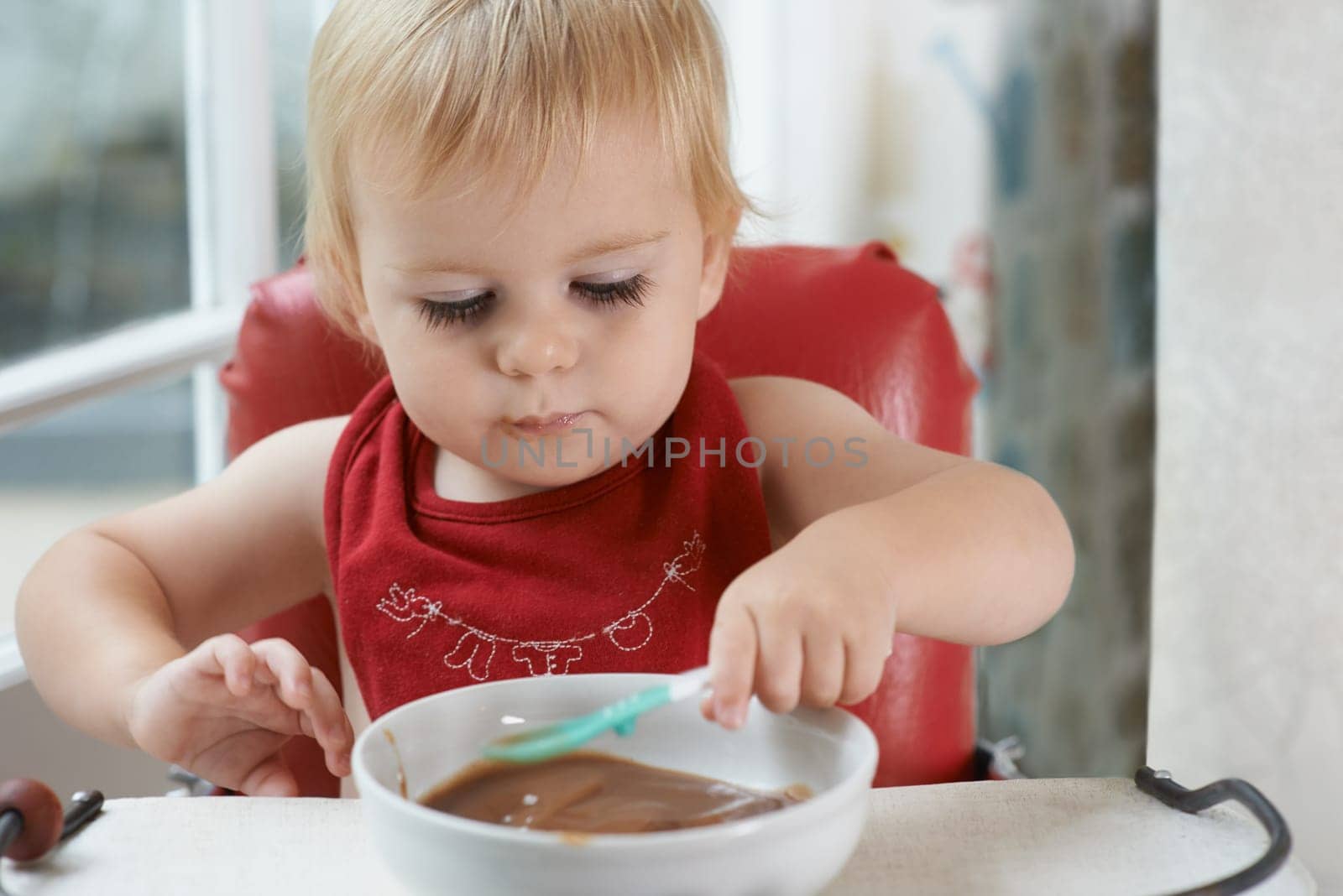 Hungry, sweet and baby eating porridge for health, nutrition or child development at home. Food, cute and girl toddler or kid enjoying an organic puree meal for lunch or dinner in high chair at house.