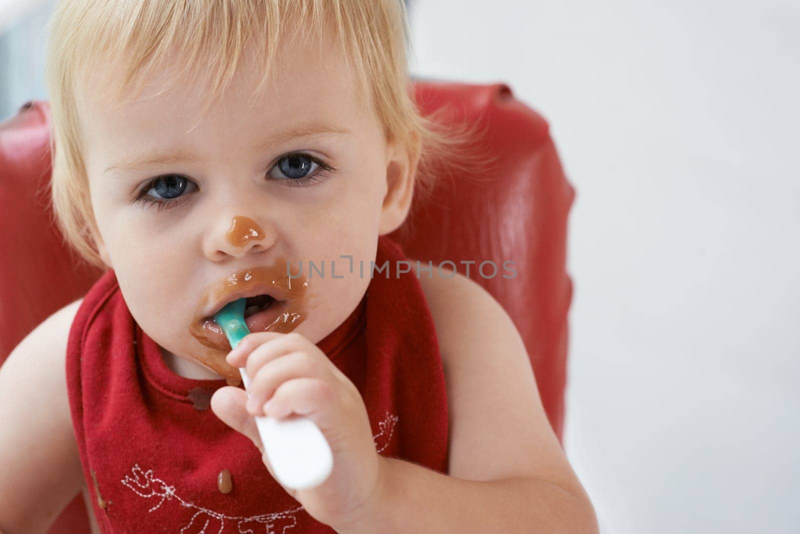 Hungry, portrait and baby eating porridge for health, nutrition or child development at home. Food, cute and girl toddler or kid enjoying organic puree meal for lunch or dinner in high chair at house.
