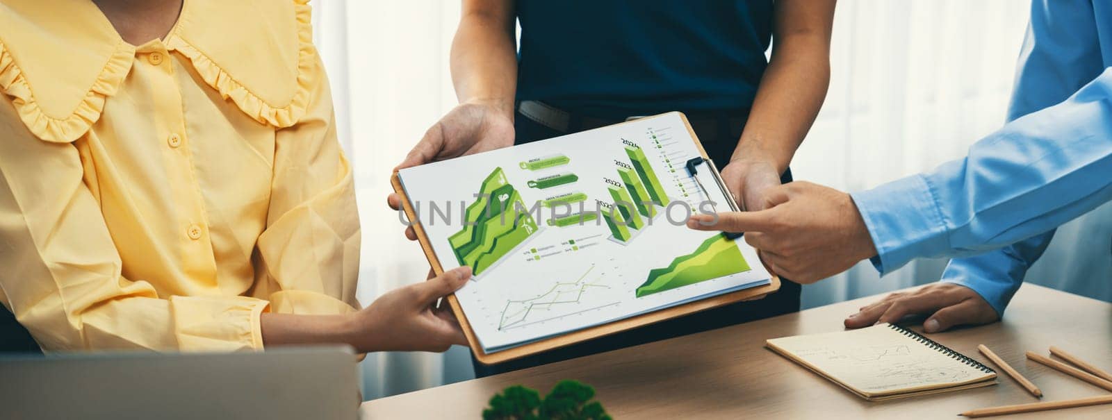 Professional business team presenting green business project by using graph to explain benefit of using renewable energy at modern meeting room. Closeup. Focus on hand. Delineation.