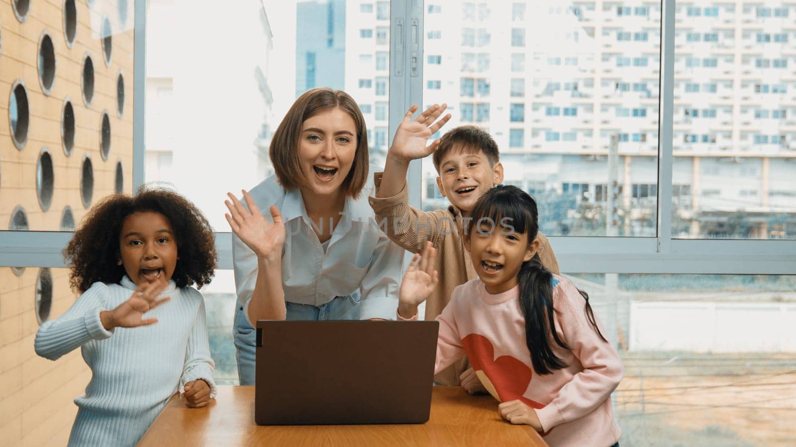 Happy caucasian teacher and multiethnic children waving hands to camera in casual uniform. Smart mentor and diverse student looking at laptop while greeting by moving hands or say good bye. Erudition.