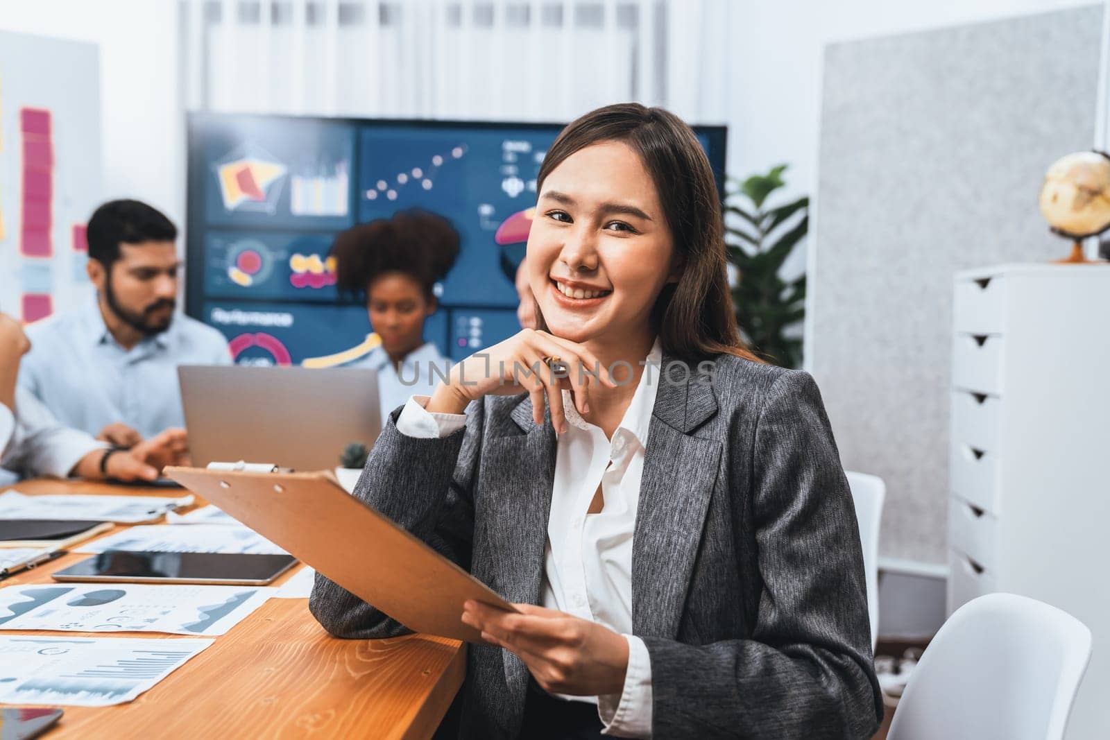 Portrait of happy young asian businesswoman with group of office worker on meeting with screen display business dashboard in background. Confident office lady at team meeting. Concord